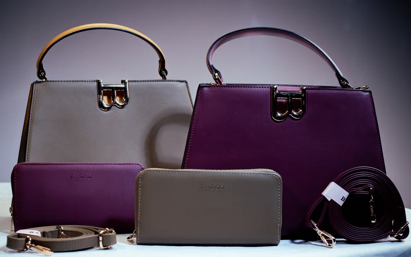 Two Bibi top-handle bags, one taupe with a mustard handle and one deep wine, with matching wallets and shoulder straps.